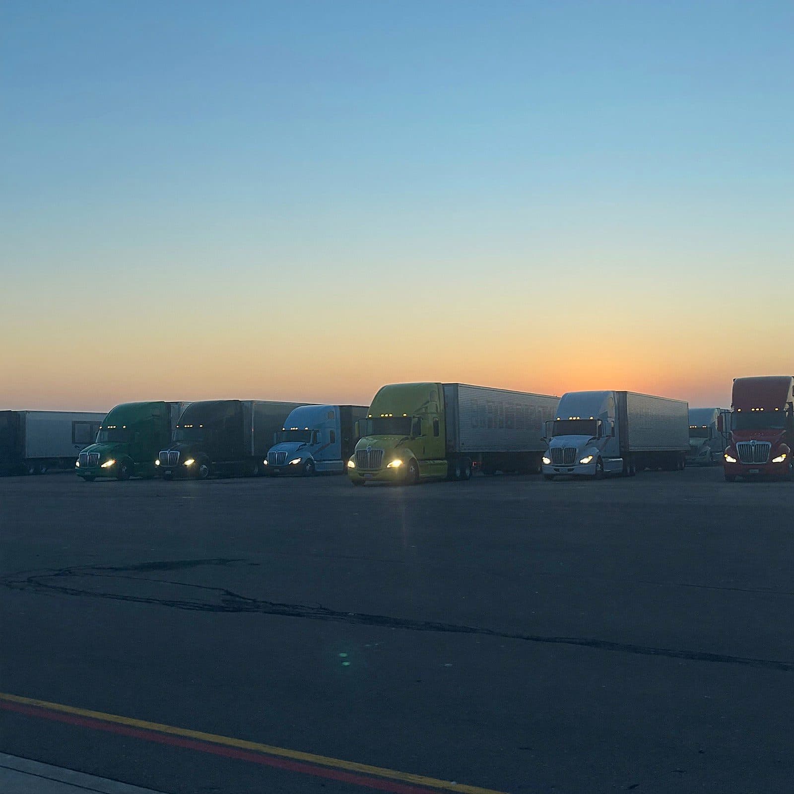 Trucks at a depot at dawn, one pulling out toward the sunrise