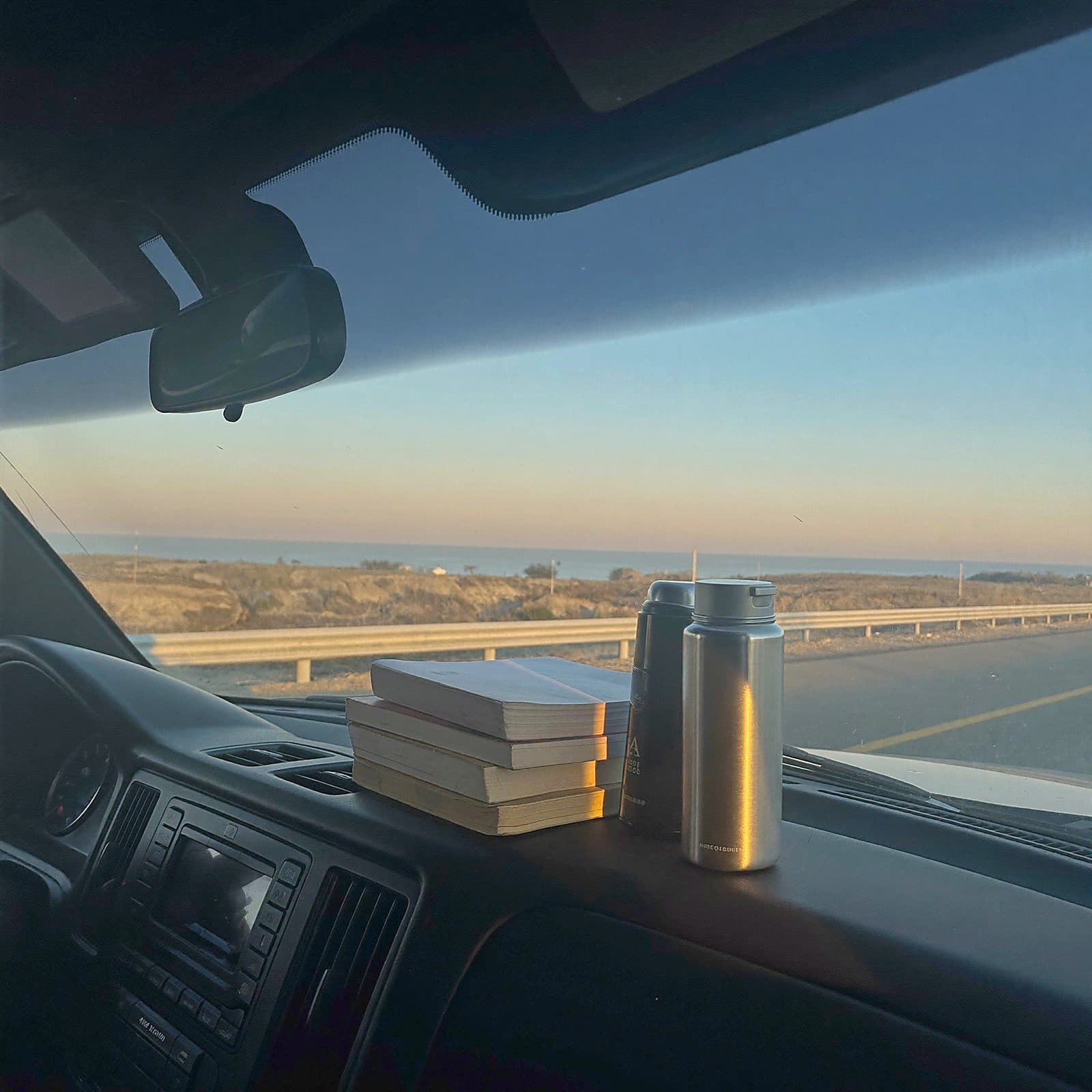 Logbooks and a thermos on a truck dashboard at dawn